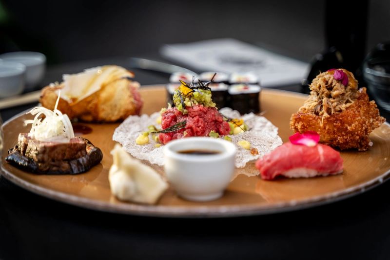 Un piatto tondo con tartare, pesce crudo, fritti e una ciotolina di salsa