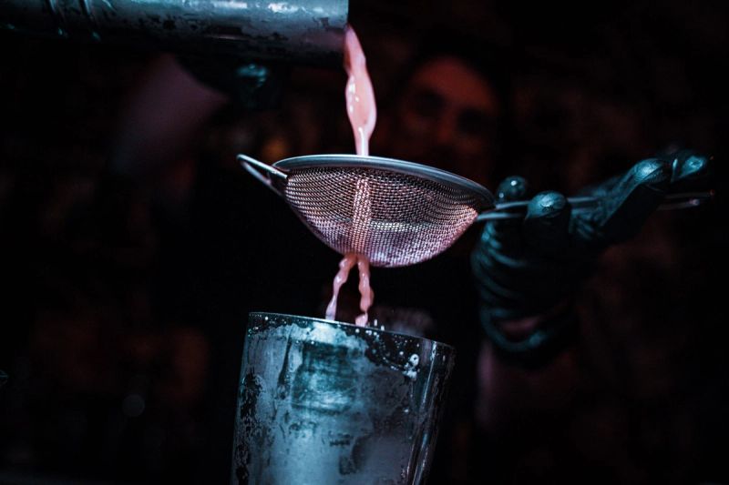 Un barman versa un cocktail attraverso un colino dentro a un bicchiere, al buio