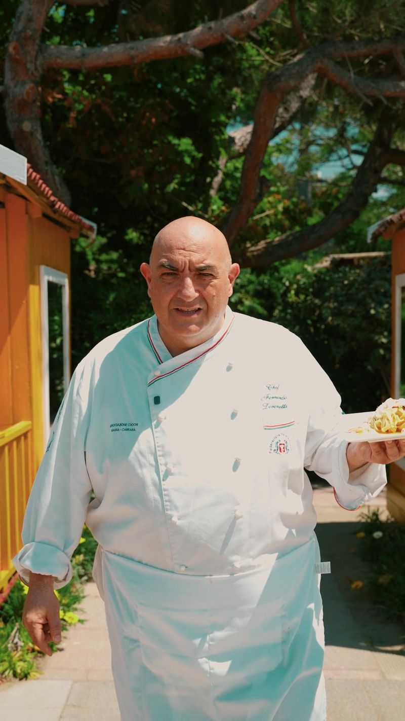 Uno chef in giacca bianca cammina in un giardino tenendo un piatto