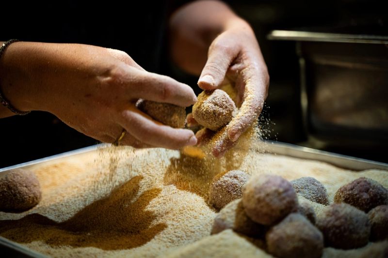 Due mani fanno rotolare delle polpette nel pangrattato dentro a una teglia