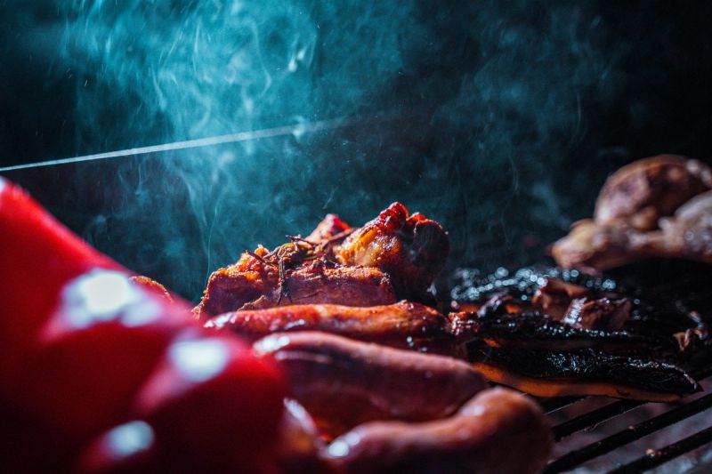 Pezzi di carne che cuociono su una griglia, con il fumo che sale