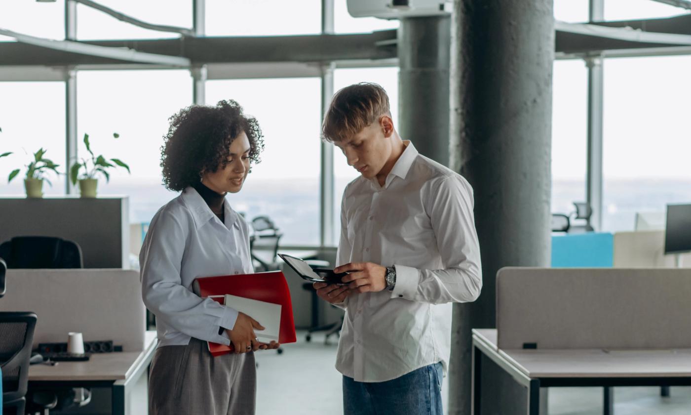 The main image for this comundo blog post about carbon accounting for SMEs shows a man and a woman in an office setting. They are looking at notes we can't see and smiling. Who knows what the notes say