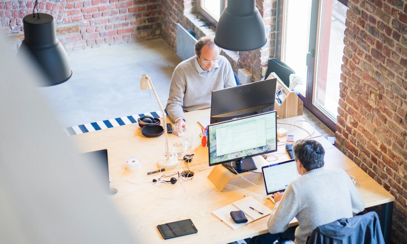 This comundo blog post about ESRS features a main image of two men working at a desk on desktop monitors. There is an exposed brick wall behind them and a large window to the side. It looks like an old industrial building.
