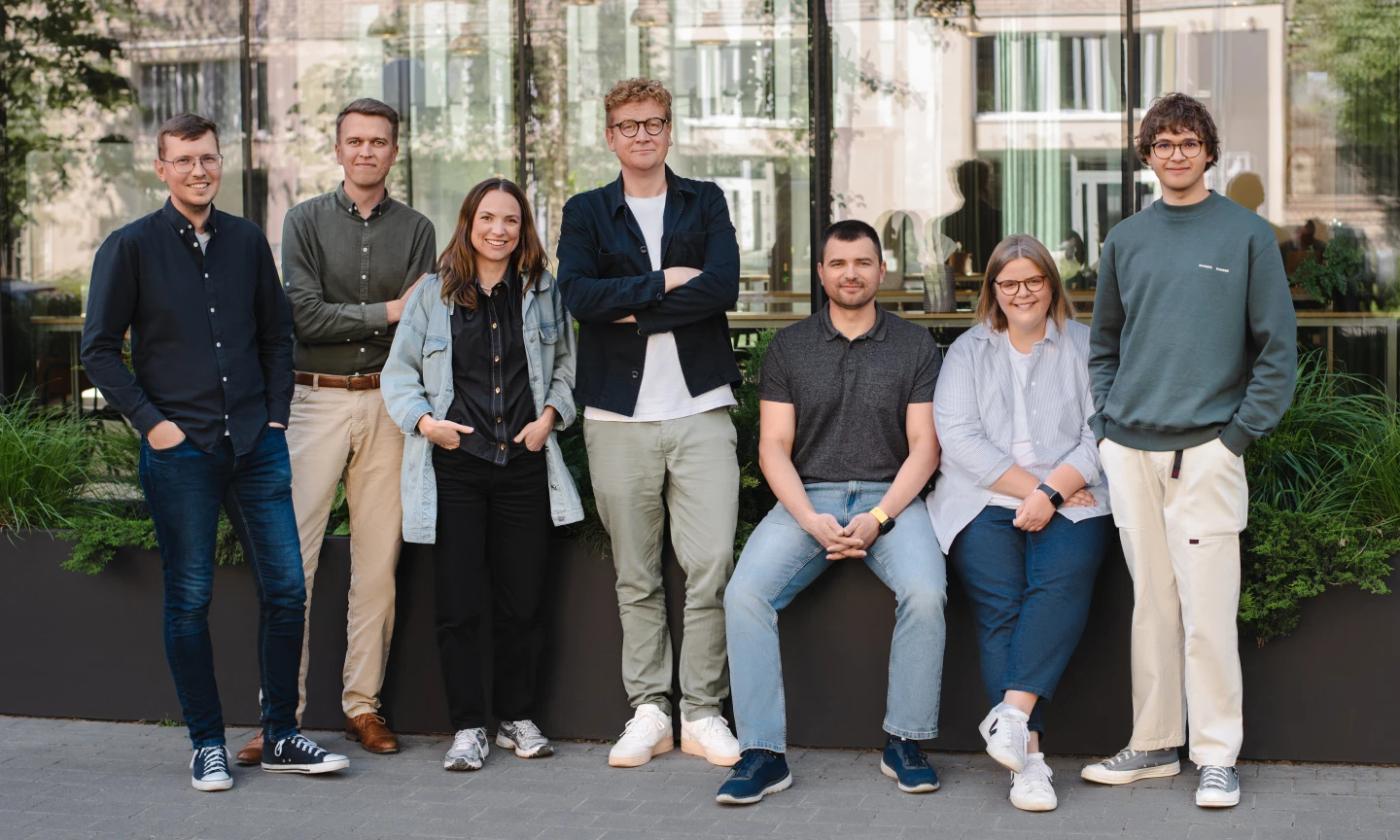 The main image for this comundo blog post about a four-day week shows a group of comundo employees. They are standing against and sitting on a small wall, looking happy and relaxed