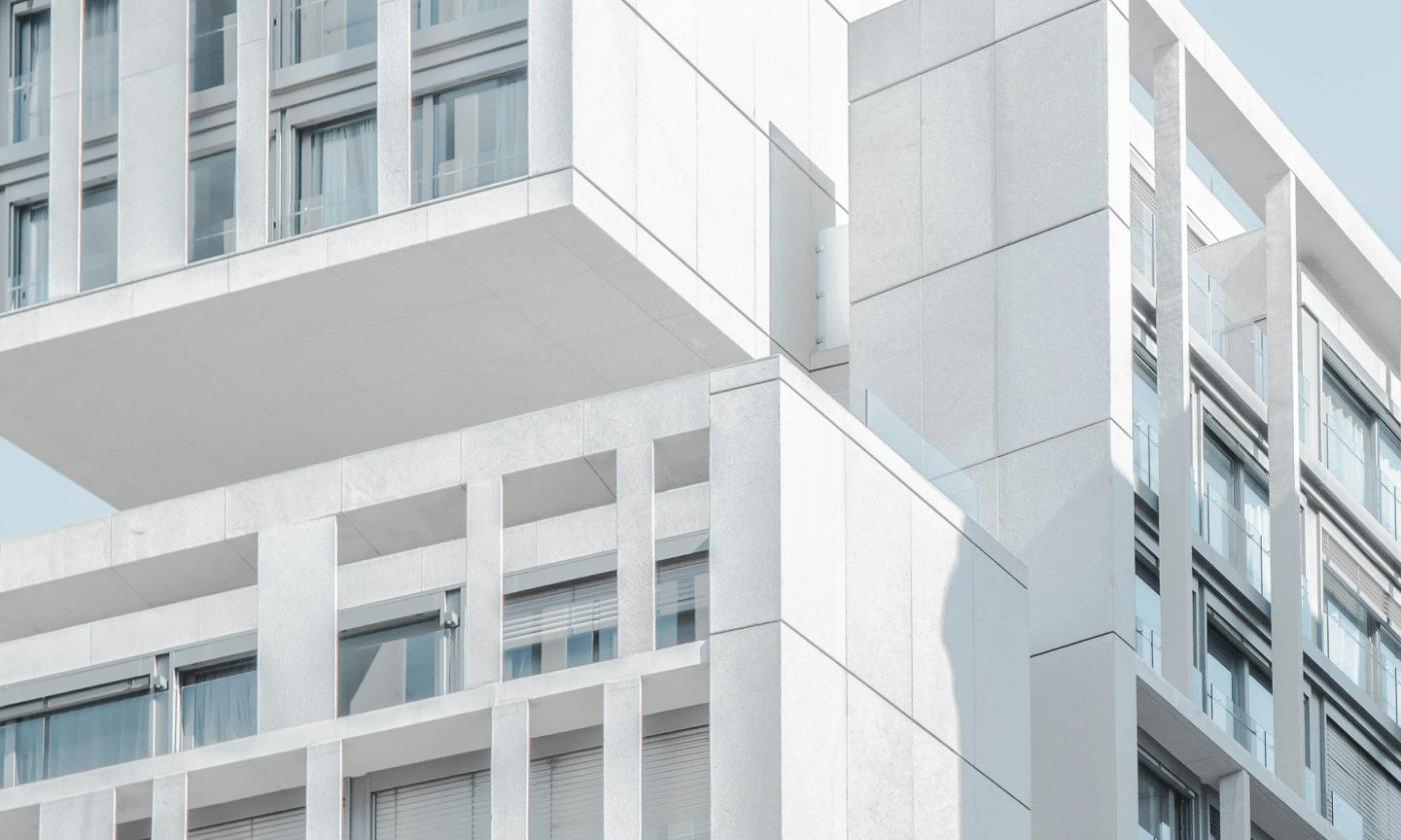 This comundo blog post about sustainability in real estate has a main image showing an apartment block. It has white walls and looks very minimalistic. We can see a sliver of blue sky in the background.