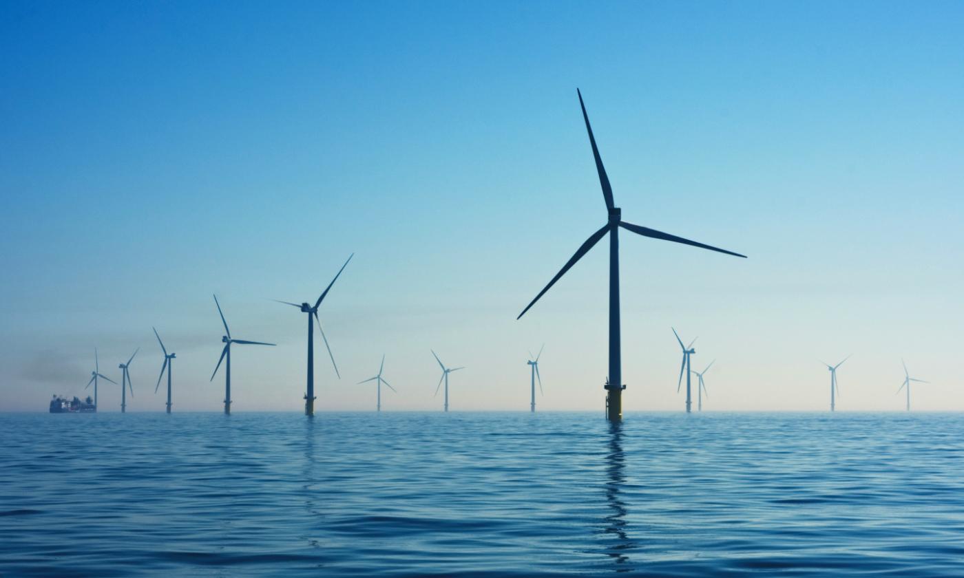 The main image for this comundo blog post shows a wind farm at sea. It's a calm sea and we can see at least 9 wind turbines. The sky is blue and it looks like a very lovely day.