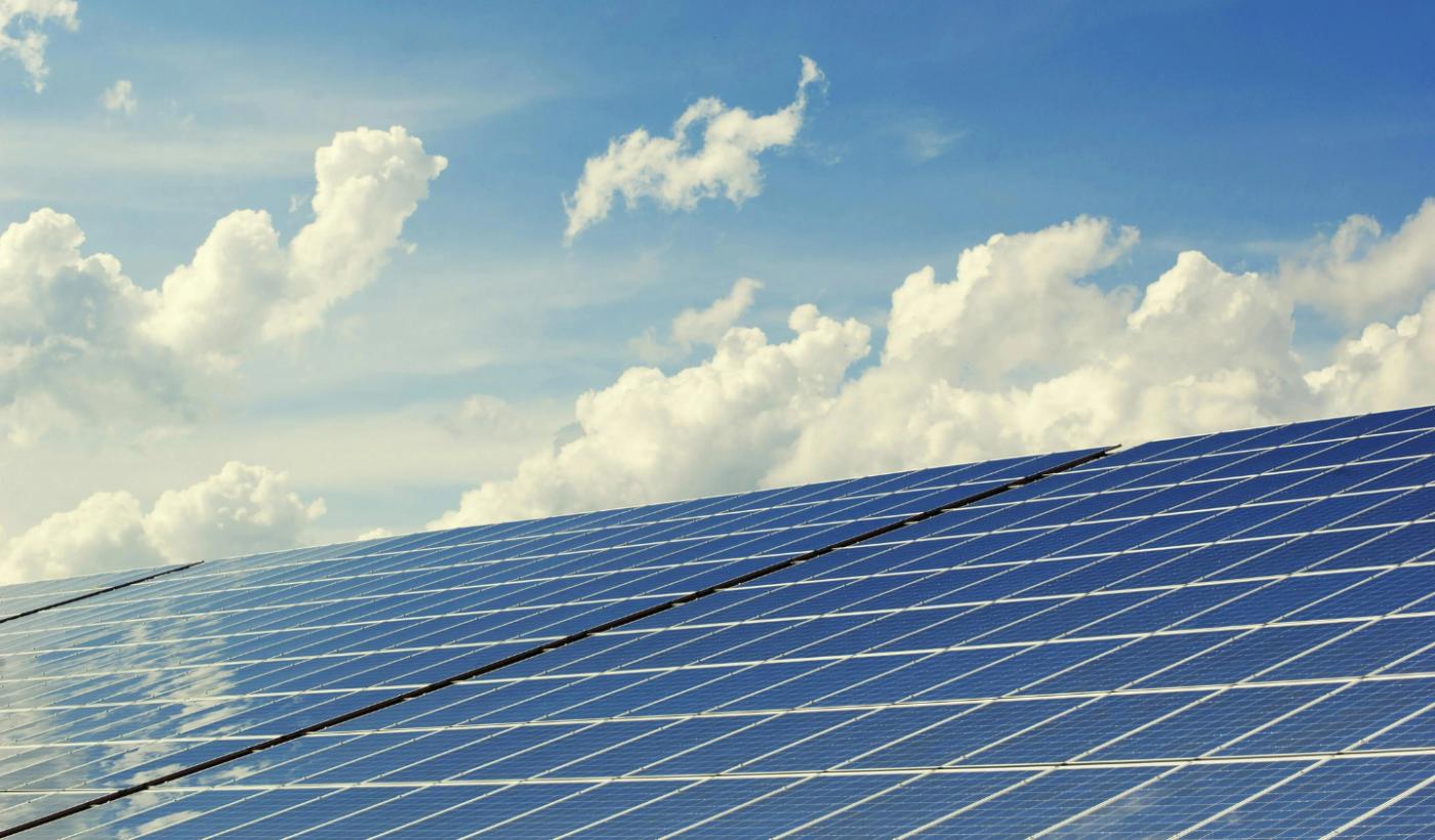 A large array of solar panels takes up the bottom half of this photo, a blue sky with fluffy clouds dominates the top half