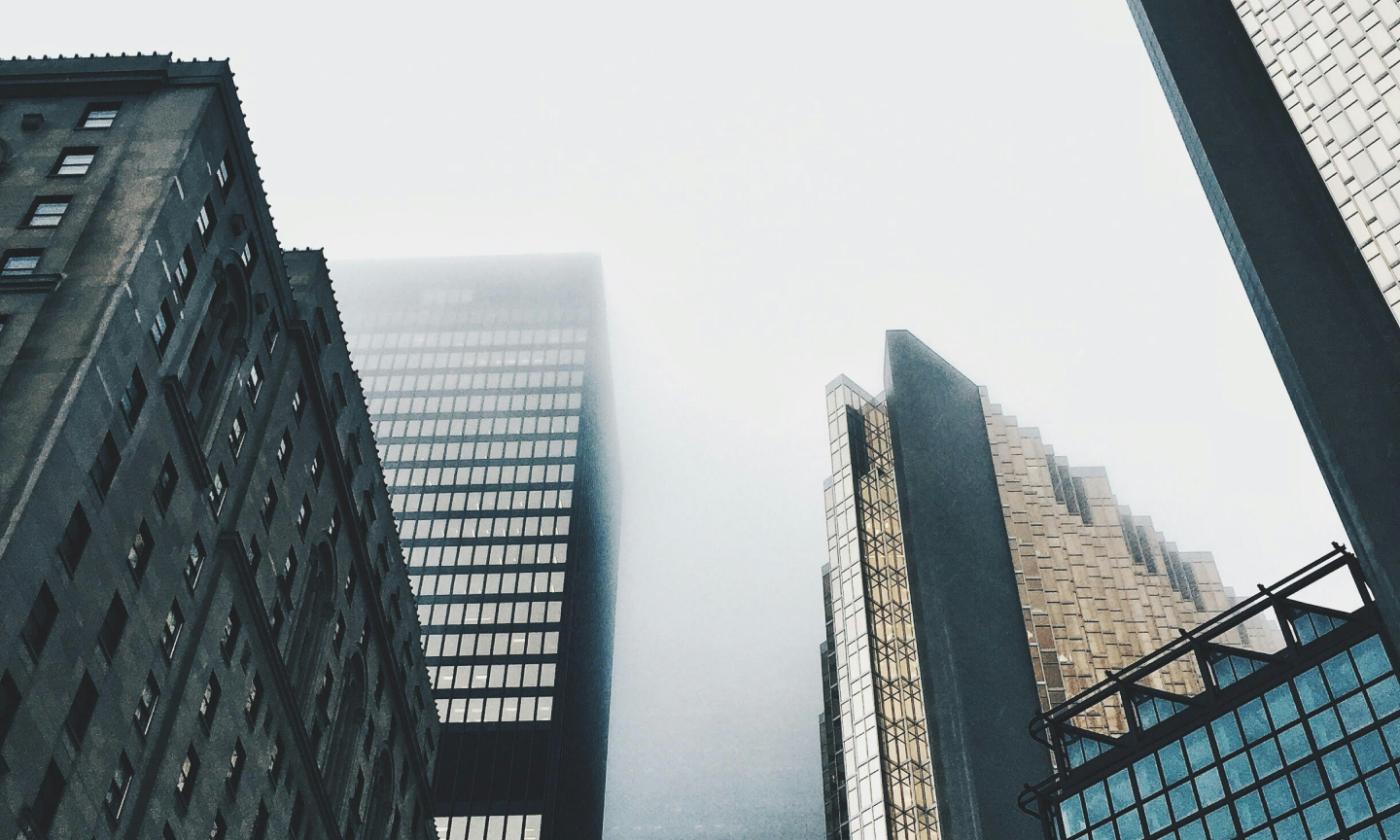 This main image for comundo's blog post about CRREM is a photo of a typical English day. It's grey and is probably raining. We're looking up towards the sky and can see some skyscrapers disappearing into the clouds.