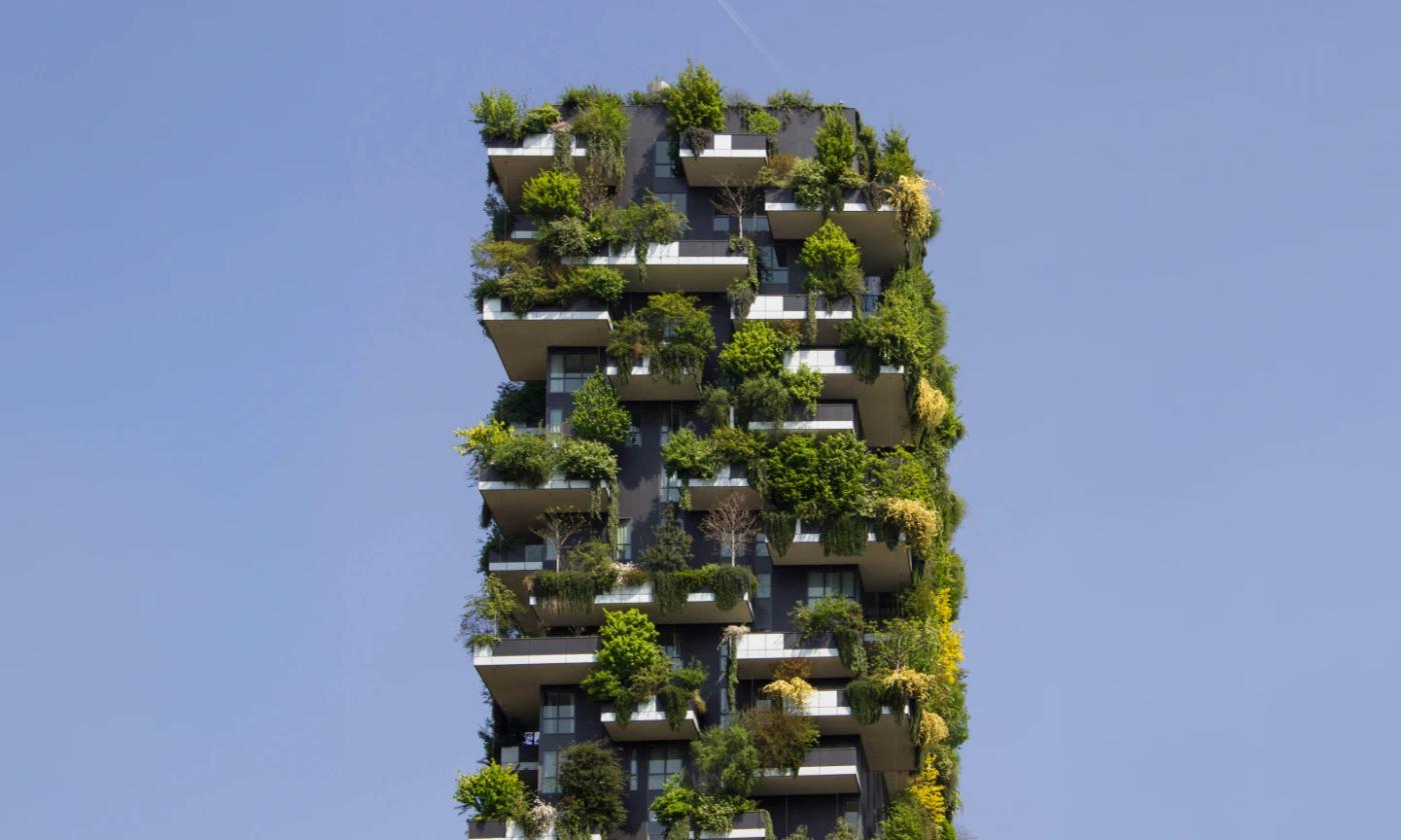 In this comundo blog post about reducing your carbon footprint, the header image is a shot of the top half of a skyscraper against a clear blue sky. The building is covered in greenery that is flowing over the end of each balcony
