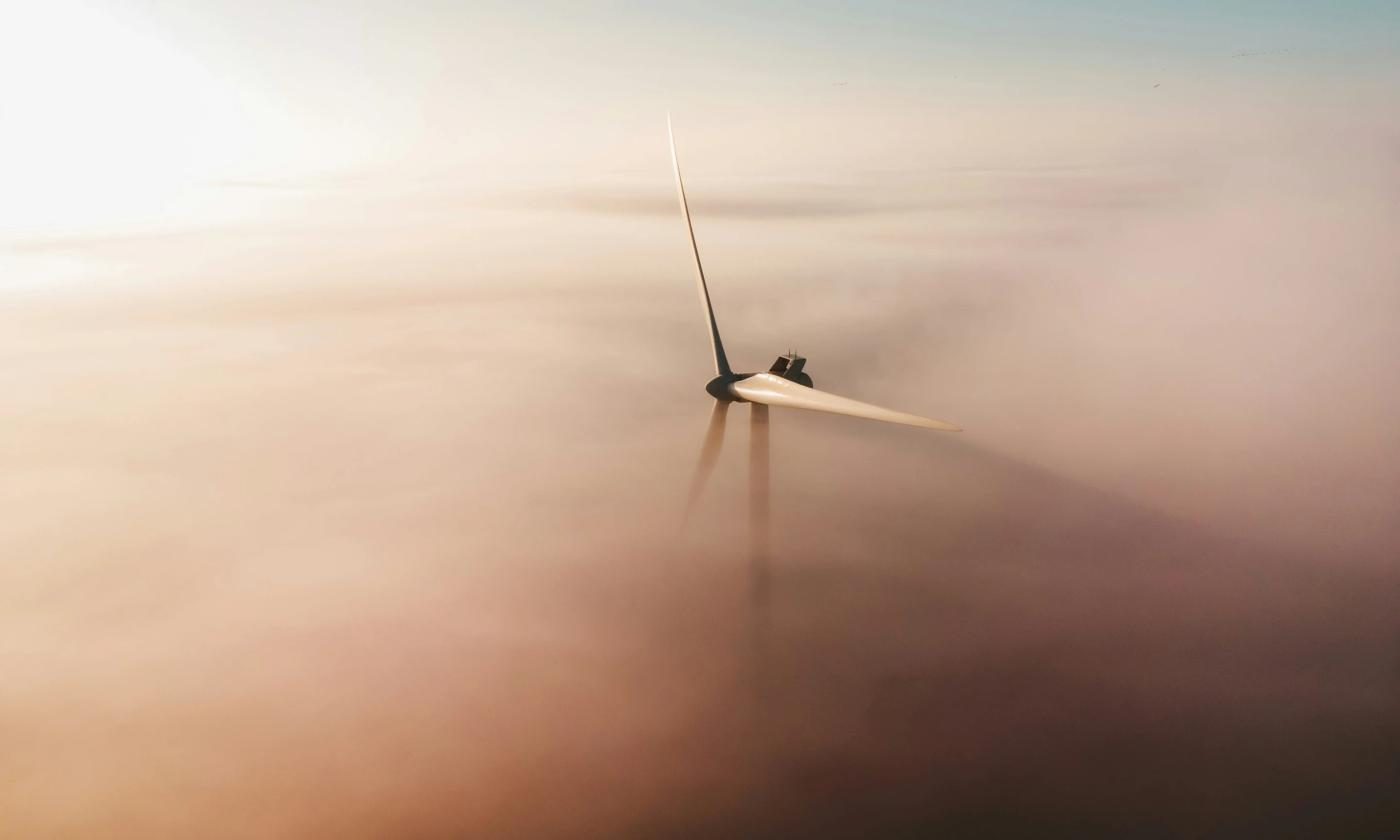 The main image for this comundo blog post about net zero shows a wind turbine just peeking through hazy pink and blue hued clouds.