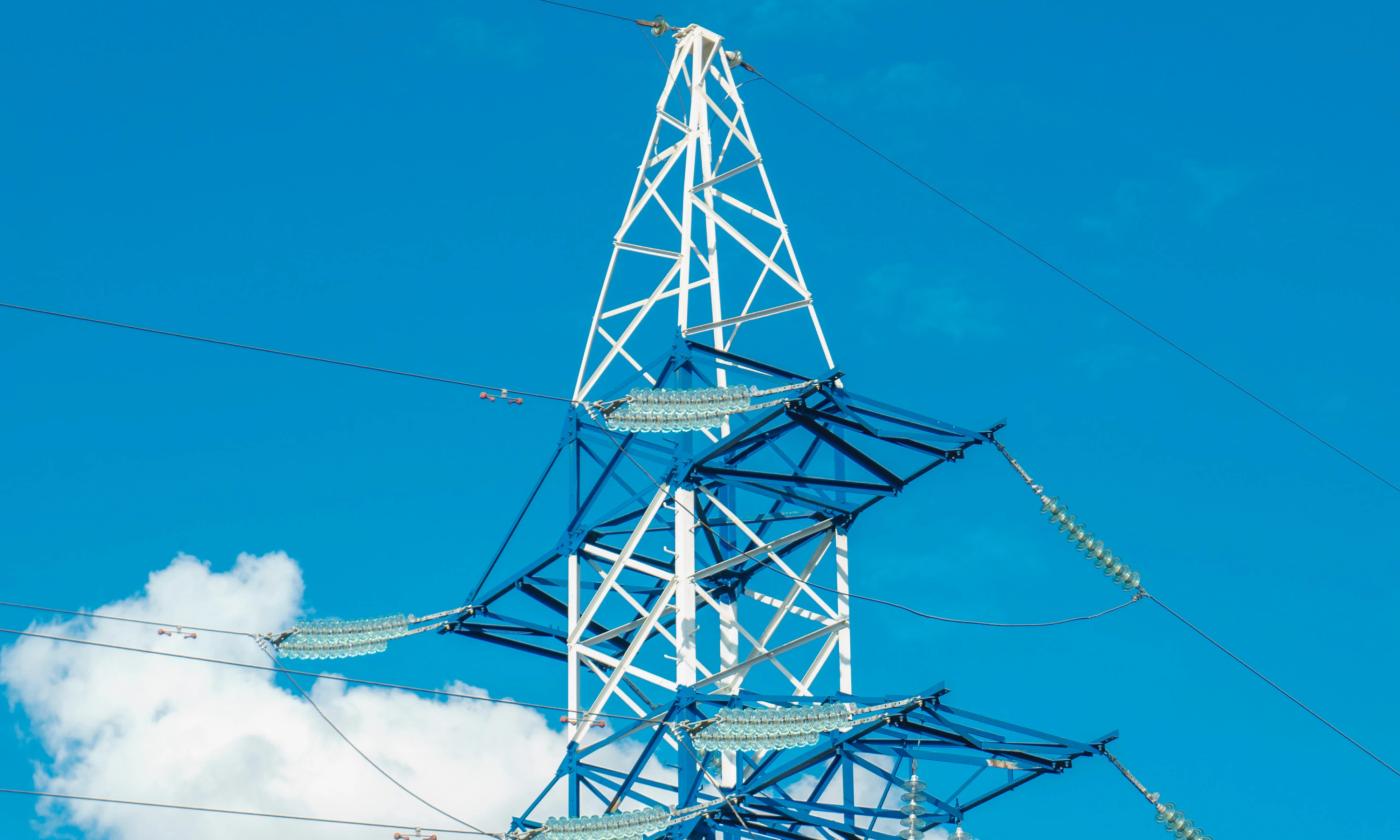 The main image for this comundo blog post about accurate carbon emission data shows a close-up of an electricity pylon. We can see the top third against a blue sky. There is one cloud in the bottom left corner