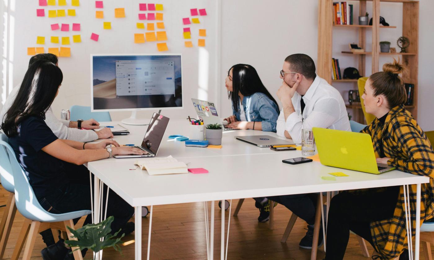 The main image for this comundo blog post shows a team of people at work, seated at at table, looking at a desktop monitor. They have open laptops and Post-Its around them.