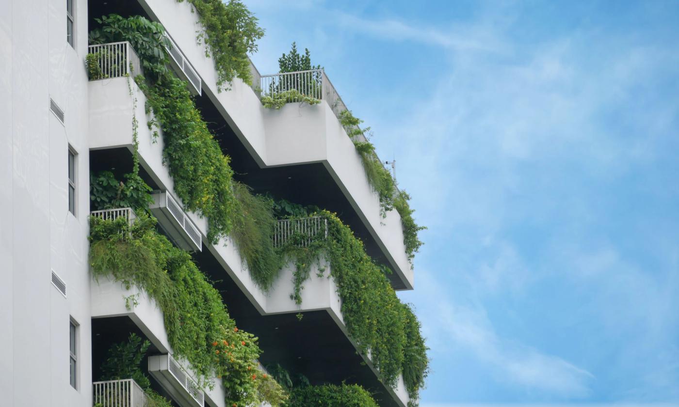This comundo blog post about building certifications has a main image showing a building with balconies. Each balcony is overflowing with greenery. The building is white, and the sky, which makes up half the image, is blue.