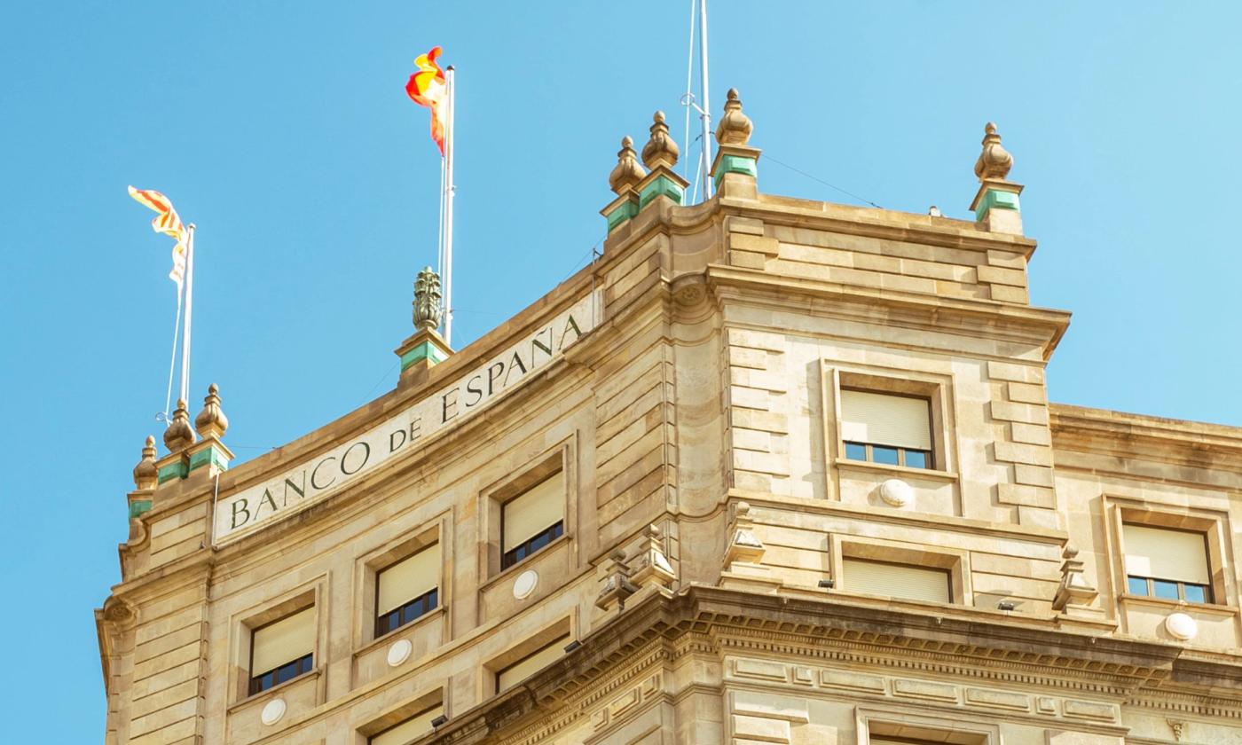 The main image for this comundo blog post about financed emissions shows the top of Banco de Espanã against a blue sky. We can see three Spanish flags blowing in the wind