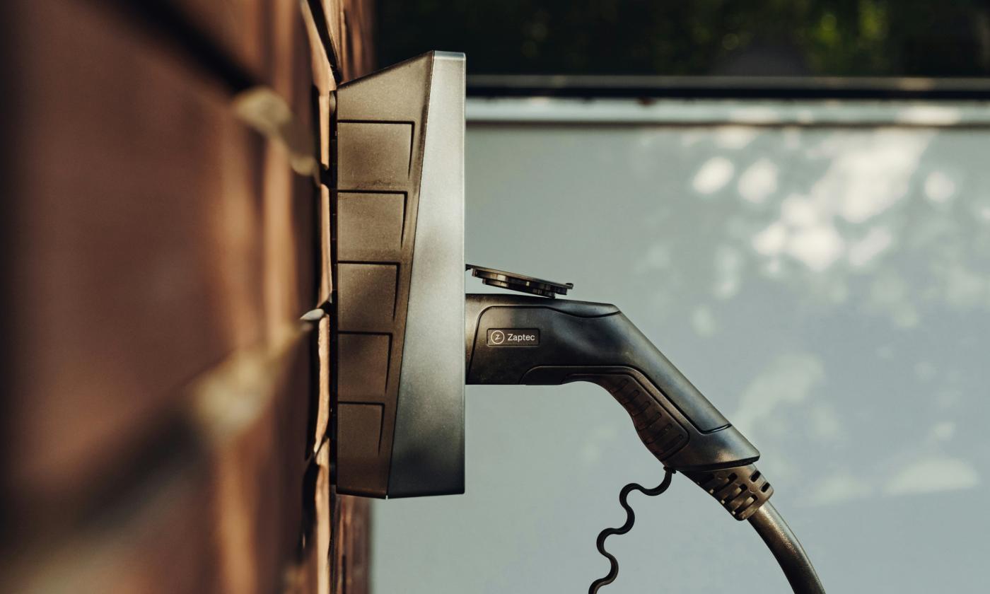 This comundo blog post about EV charger overload has a primary image that shows a close-up photo of an EV car charger plugged into an electrical output.