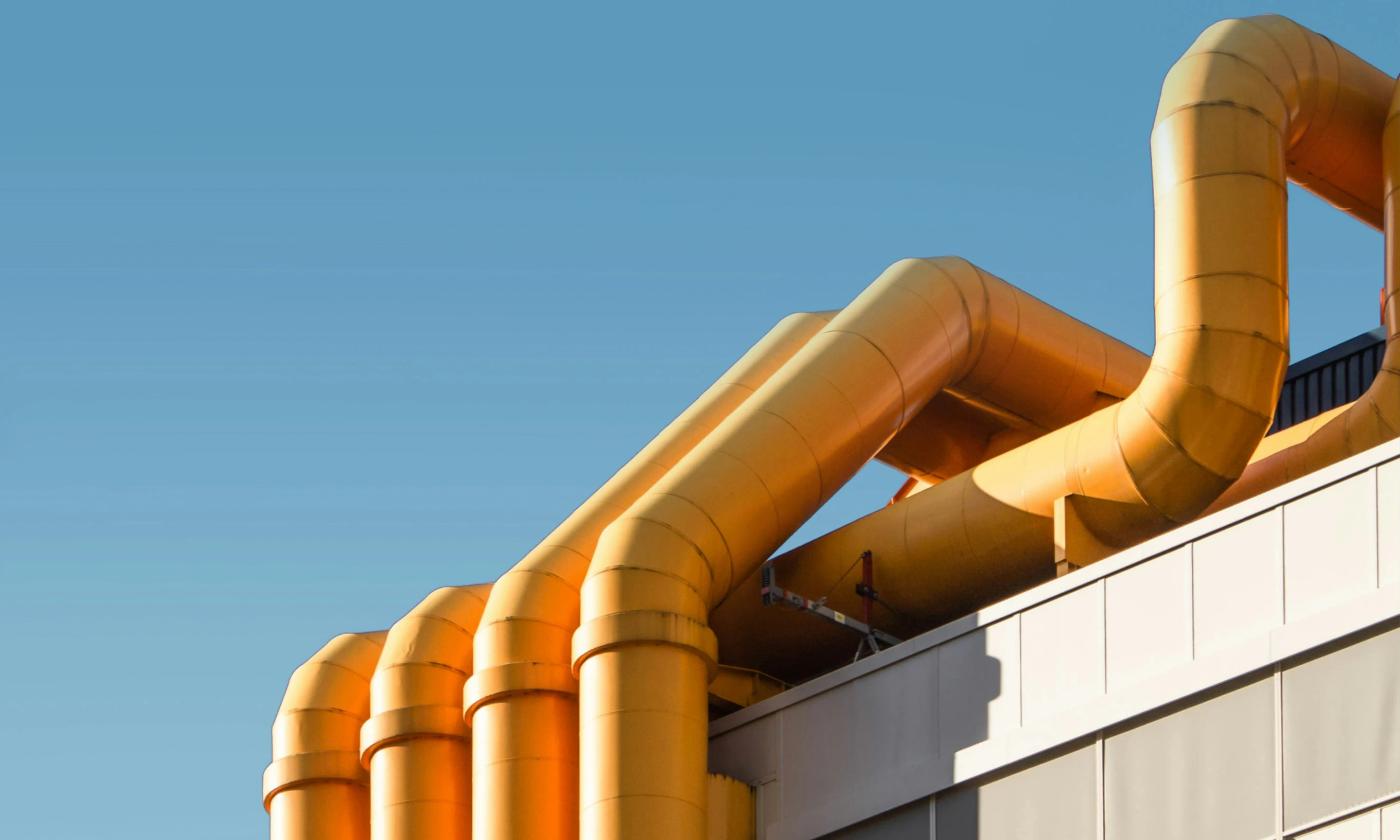 The main image for this comundo blog post about CSDDD is a close-up photo of the top of a building. We can see blue sky in the background and some yellow ventilation pipes creeping over the top of the building in the foreground