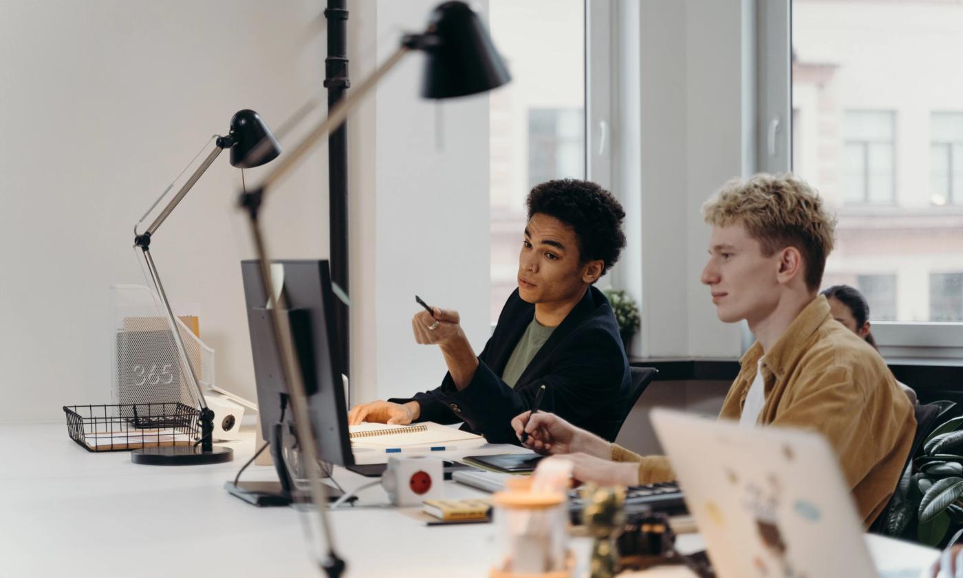 This comundo blog post about CSRD has a feature image that shows a young man and woman working at office desks. It's a light and pleasant looking office, with a window behind them and lamps on the desks.