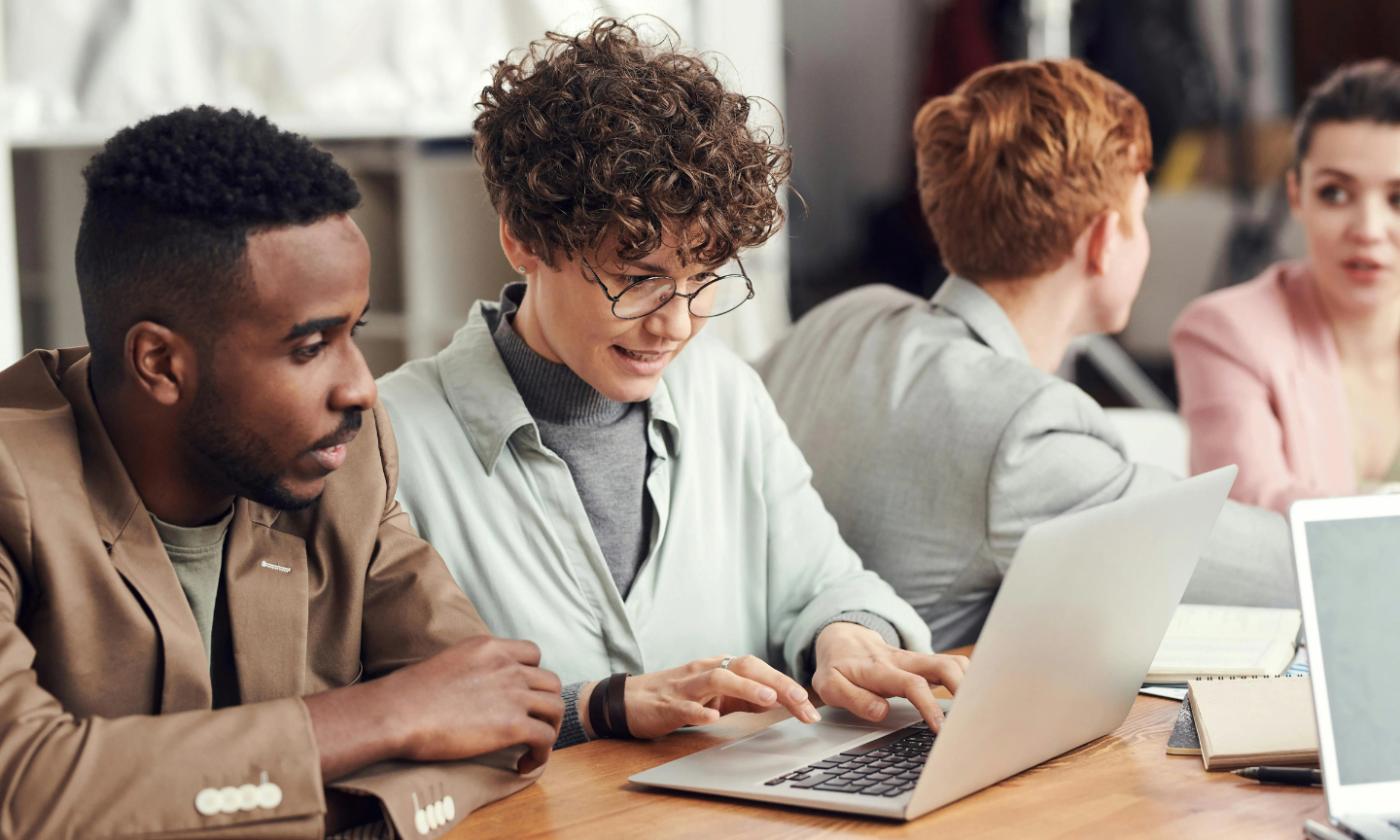 The main image of this comundo blog post shows a young and diverse team of people sitting at a table. The two people in the foreground are sharing a laptop and working at something we can't see. It must be comundo because they look very happy.