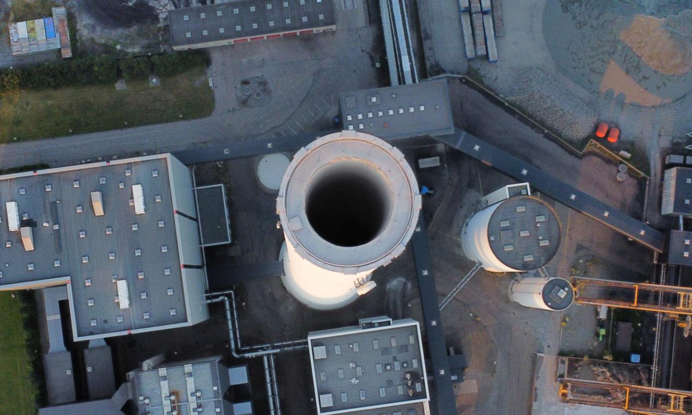 The main image for this comundo blog post about the GHG Protocol and Scopes 1, 2 and 3 is an aerial shot of an industrial steam chimney. We're looking directly down into it but there is no steam coming out of it. Next to the chimney, we can see the roofs of a few other buildings.