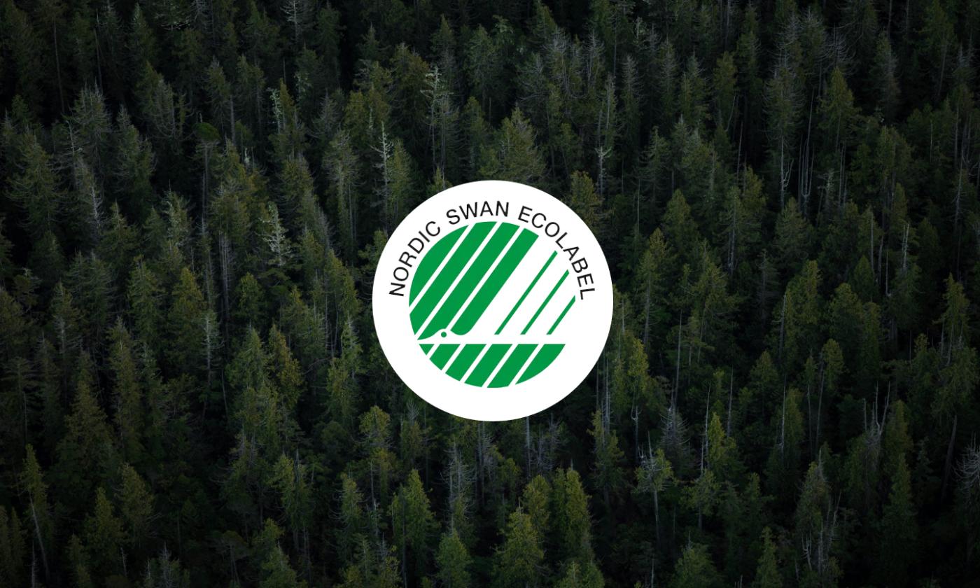 The main image for this comundo blog post about the Nordic Swan Ecolabel is the Nordic Swan Ecolabel logo superimposed on an aerial view of a fir tree forest