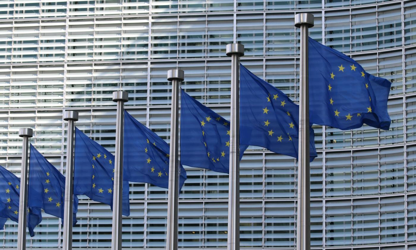 The main image for this comundo blog post about EU legislation shows seven EU flags outside of the EU's headquarters in Brussels. All we can see of the building is windows