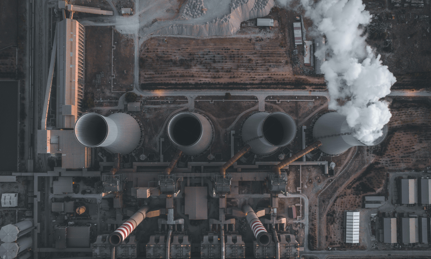 The main image for this comundo blog post about carbon accounting shows an aerial view of an industrial area. We can see four smoke stacks, one of which is operating, and other buildings surrounding them