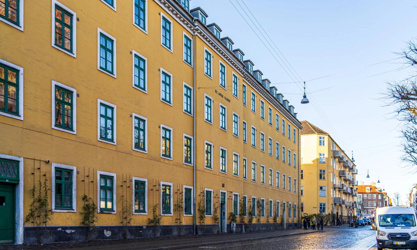 This comundo blog post about scope 3 emissions features a main image showing a typical Copenhagen block of flats stretching into the distance. The building is yellow, and there is a blue sky behind. In the foreground, we can see the road and van parked on one side.