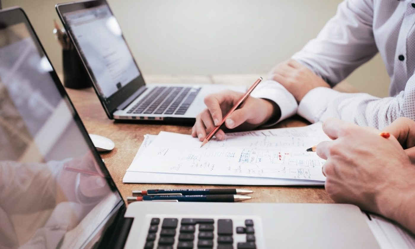 This comundo blog post about the importance of EPCs, shows two people working at a desk. We can only see their hands and forearms, and that they're working on laptops and some important looking paper in front of them. 