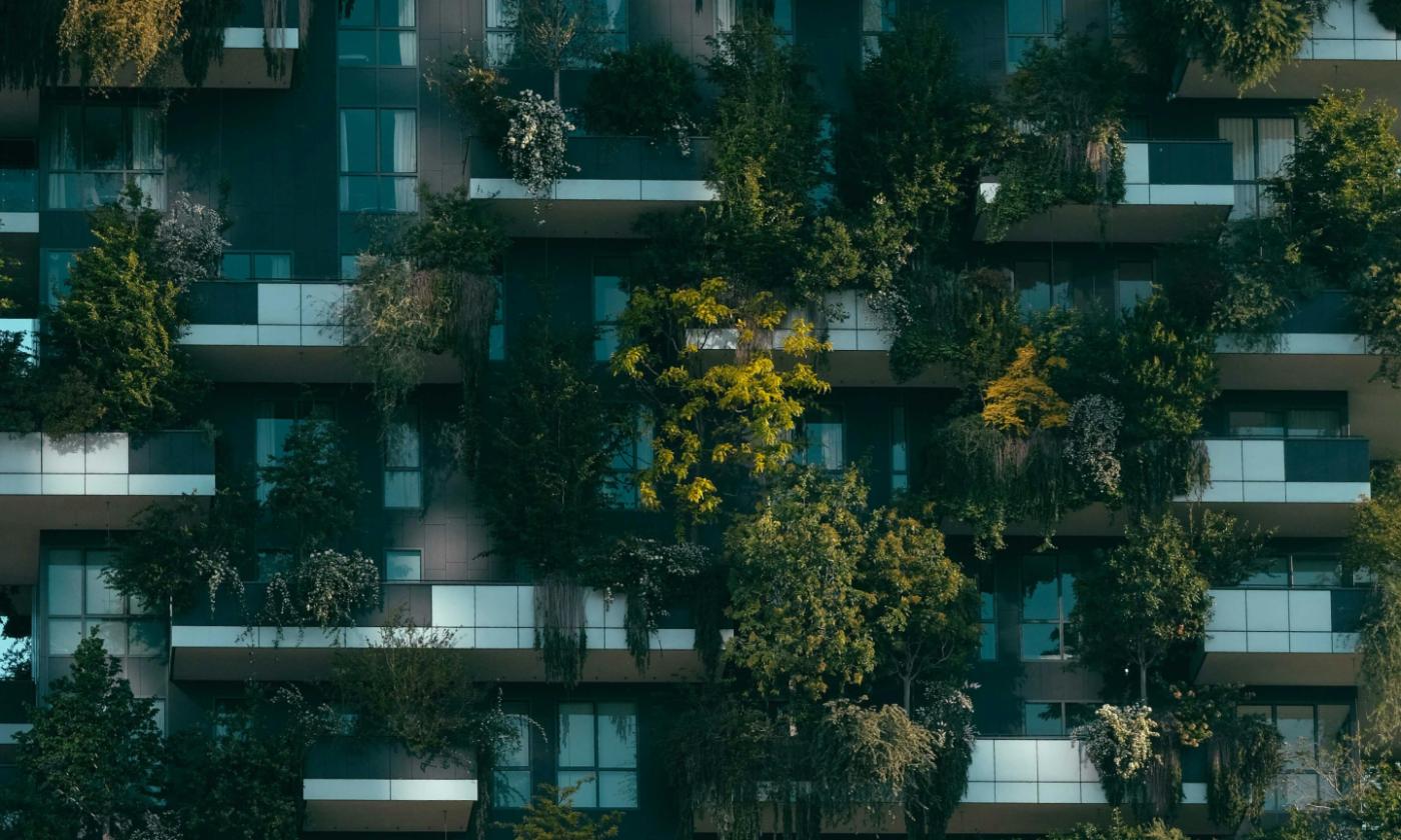 This image is a close-up of the side of a building. We can see multiple balconies, each of which have plenty of hanging plants. 