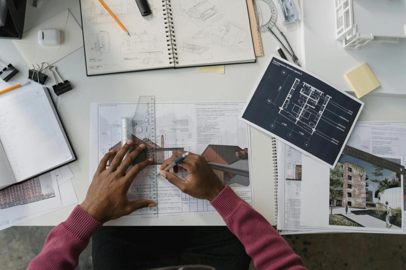 The main image of this comundo blog post is a photo of a desk covered in blue prints, and other work paraphernalia, and a pair of hands at work. We're looking at the desk from above, so can't see the floor or any more of the person, other than their hands.