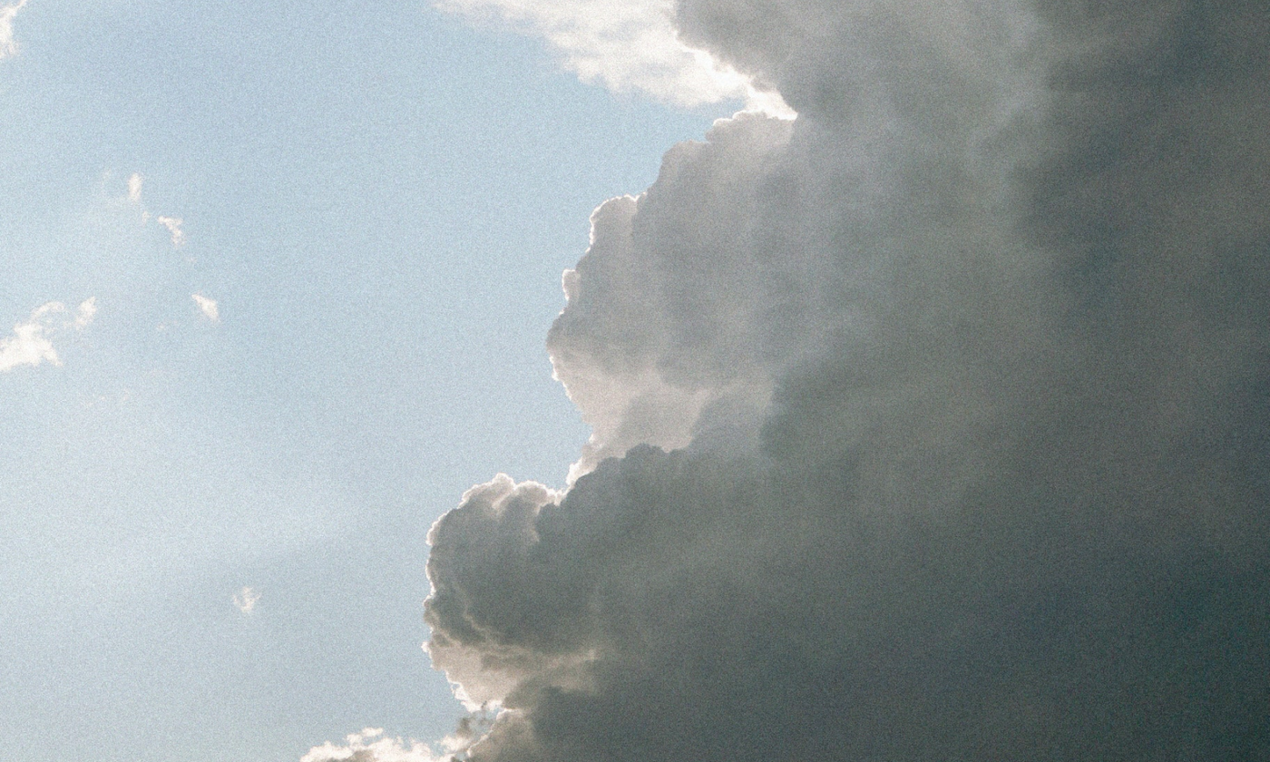 The main image for this comundo blog post about the evolution of carbon accounting standards shows sunbeams coming through a dark cloud to the right of the image. To the left, the sunbeams are lost against the blue sky