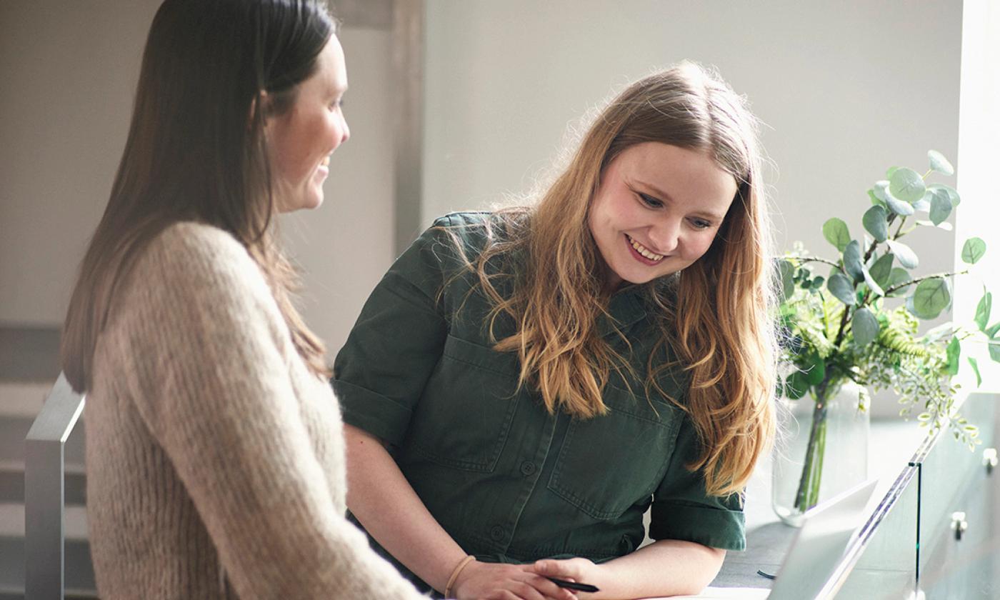 The main image for this comundo blog post about the four-day week shows two women looking at a laptop. They are both standing up and smiling although we can't see what they are looking at