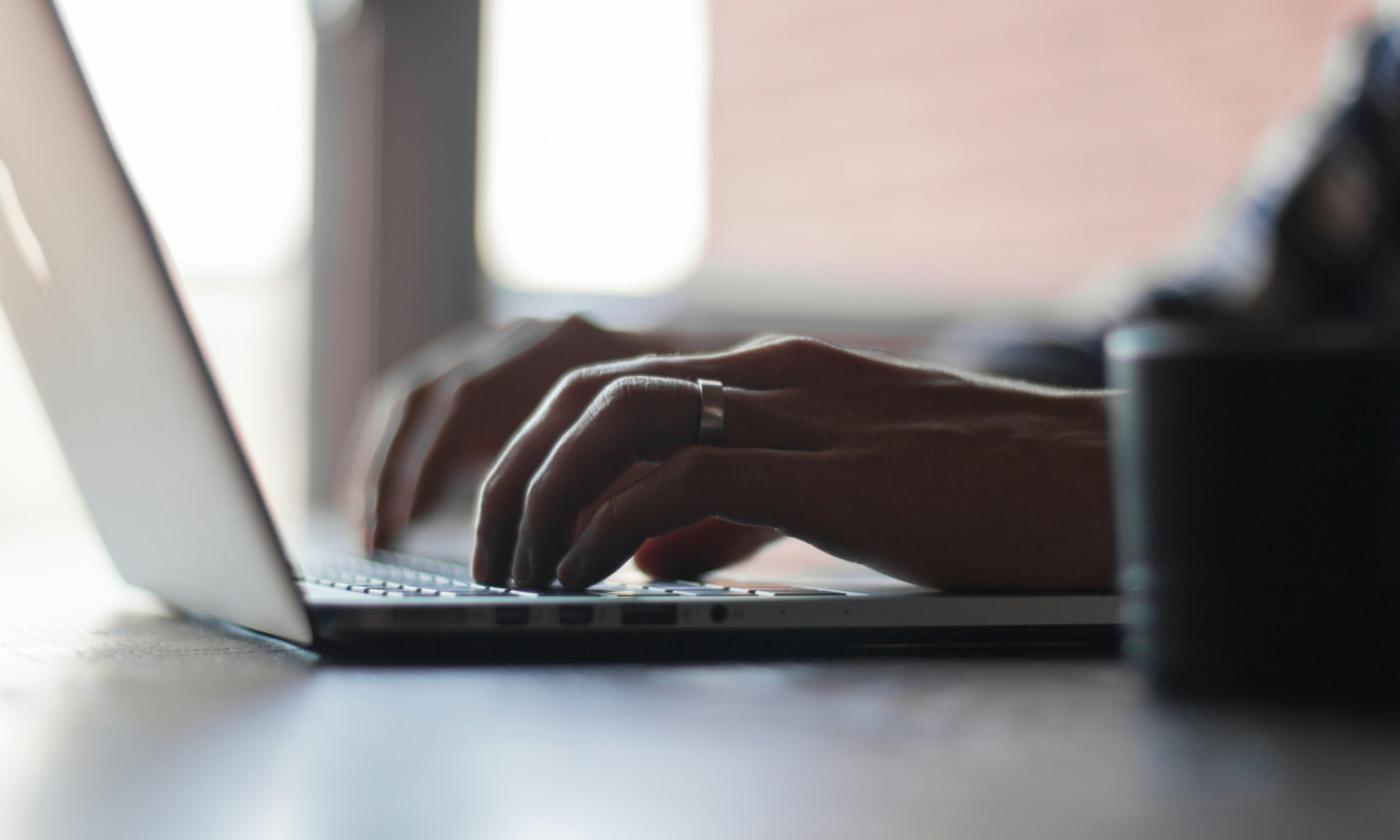 This comundo blog post about cost benefits of an all-in-one carbon accounting solution is a close-up shot of someone's hands typing on a laptop.