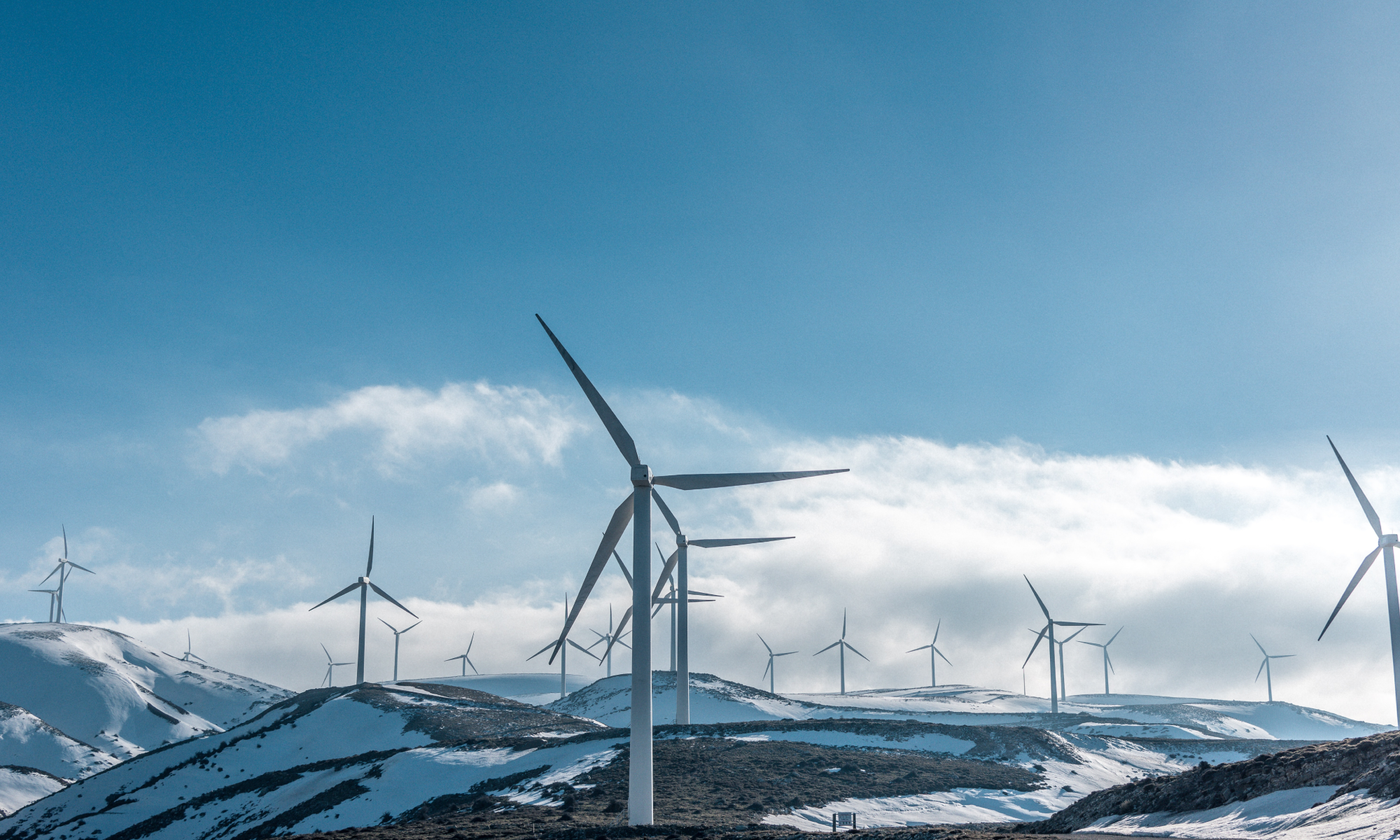 The main image for this comundo blog post about net-zero emissions shows a snowy and undulating landscape dotted with multiple wind turbines. It looks cold but also quite awe-inspiring