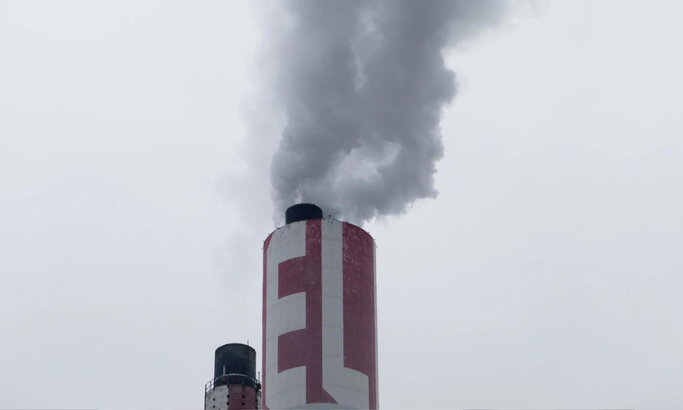 A close-up photo of a smoke stack against a light grey sky