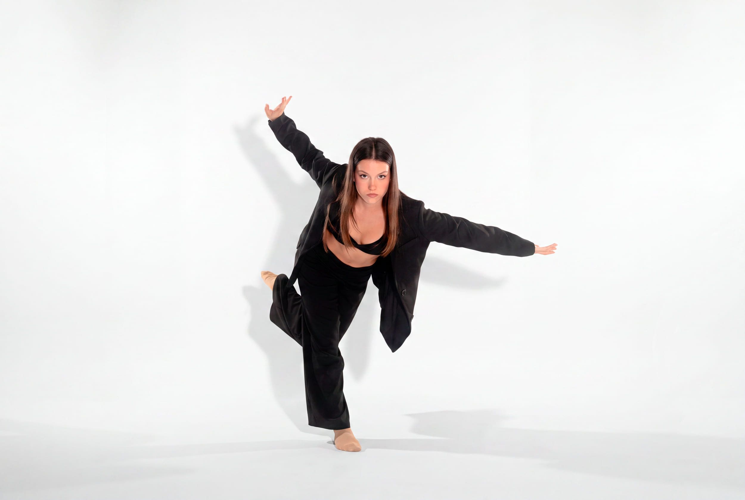 Ballerina in giacca nera in una posa di danza modern, in appoggio su una gamba