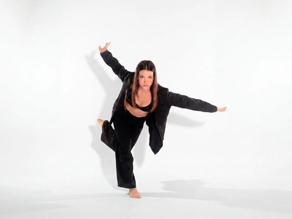 Ballerina in giacca nera in una posa di danza modern, in appoggio su una gamba