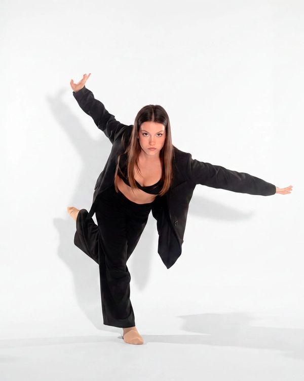 Ballerina in giacca nera in una posa di danza modern, in appoggio su una gamba
