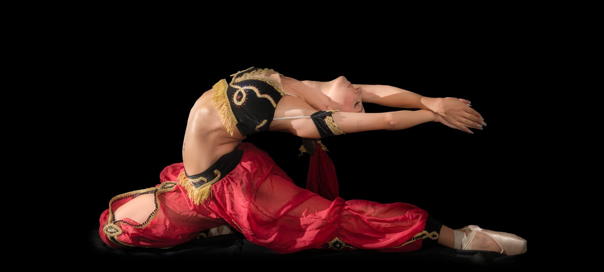 Ballerina in costume rosso e oro distesa a terra in una posa di repertorio