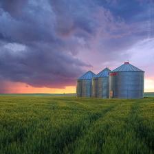 Grain silos in a field under a brooding sky at sunset