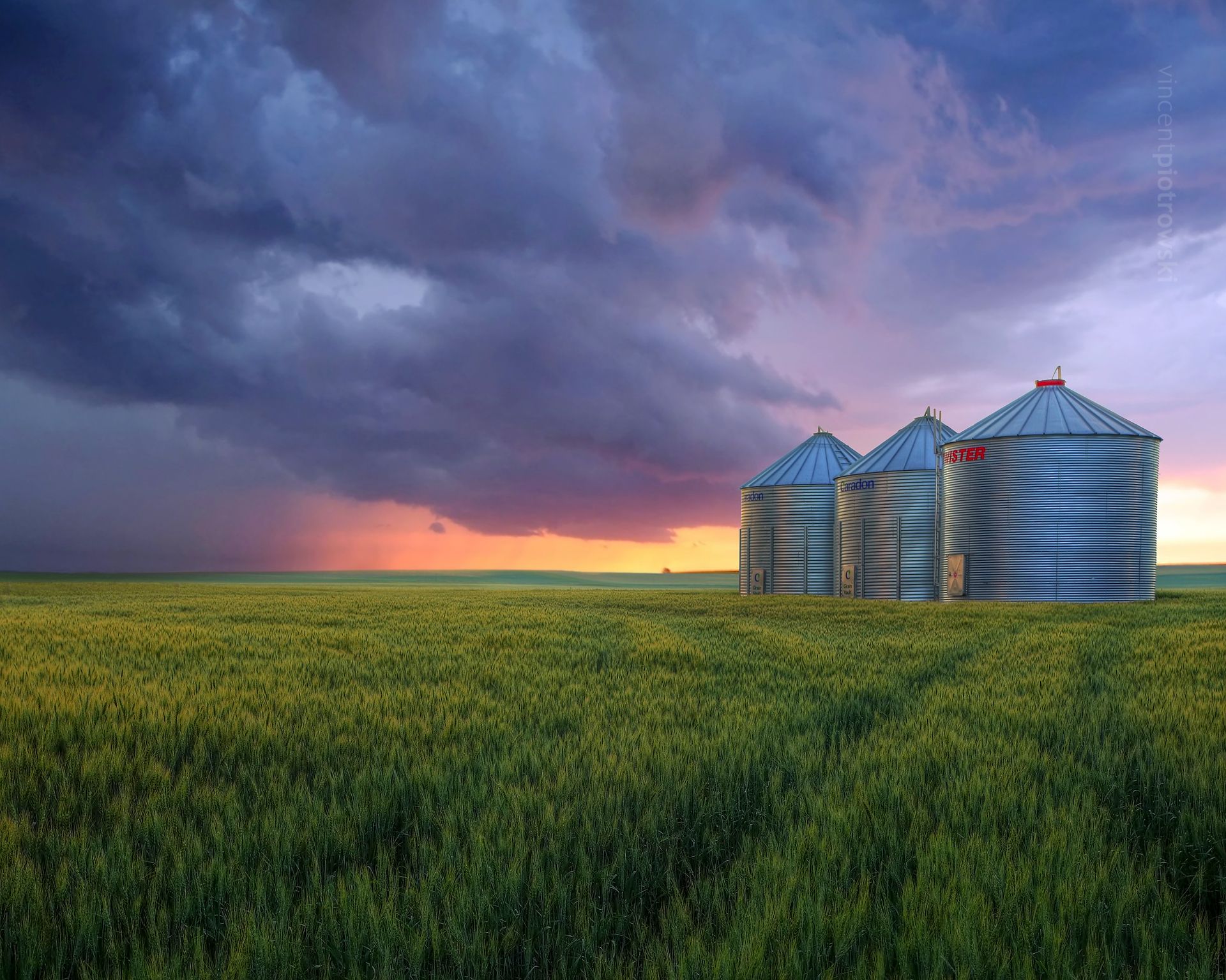 Grain silos in a field under a brooding sky at sunset