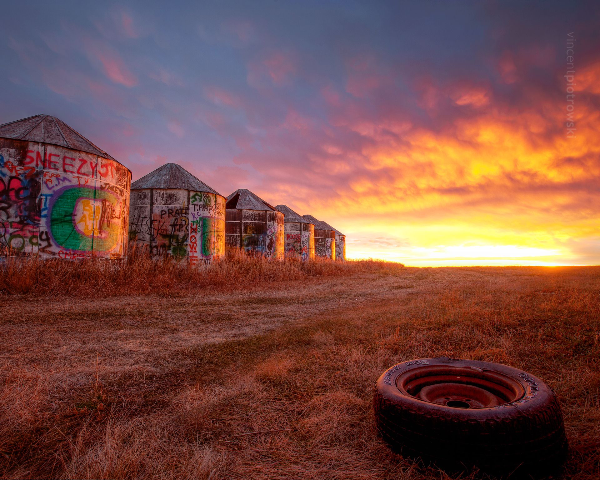 An intense sunrise behind old wooden grain silos on the prairies