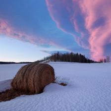 A round bale of hay in the snow under a spectacular cloud formation