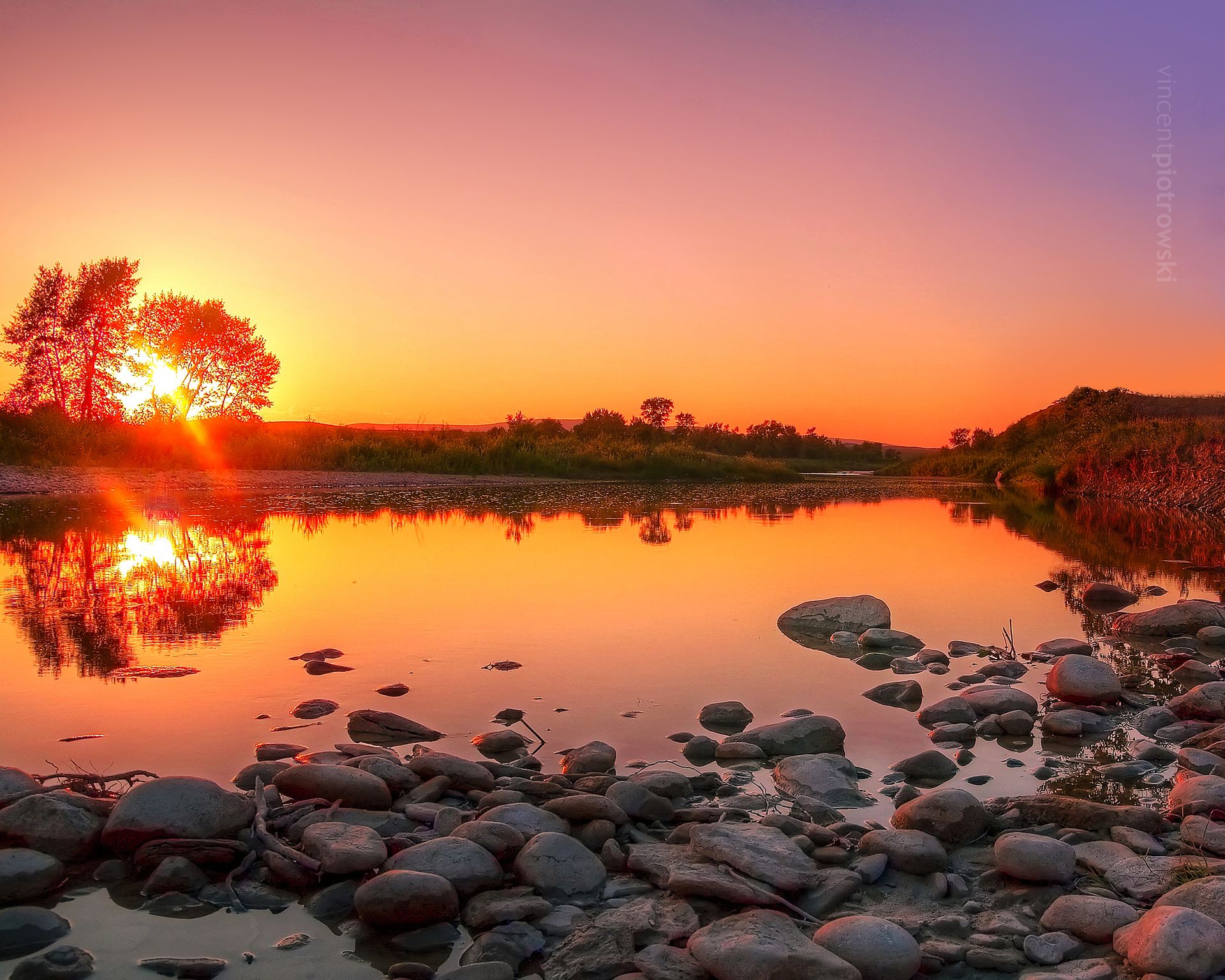 Sun setting behind a tree over a dammed up part of Willow Creek Alberta