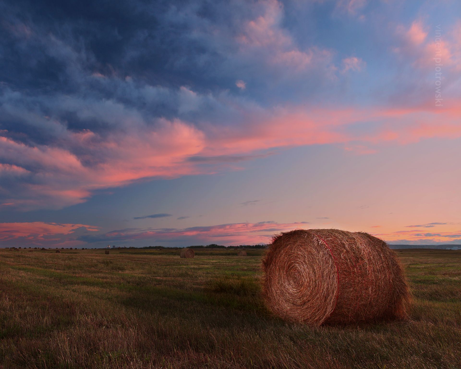 A round bale sitting under an interesting cloud formation at sunset
