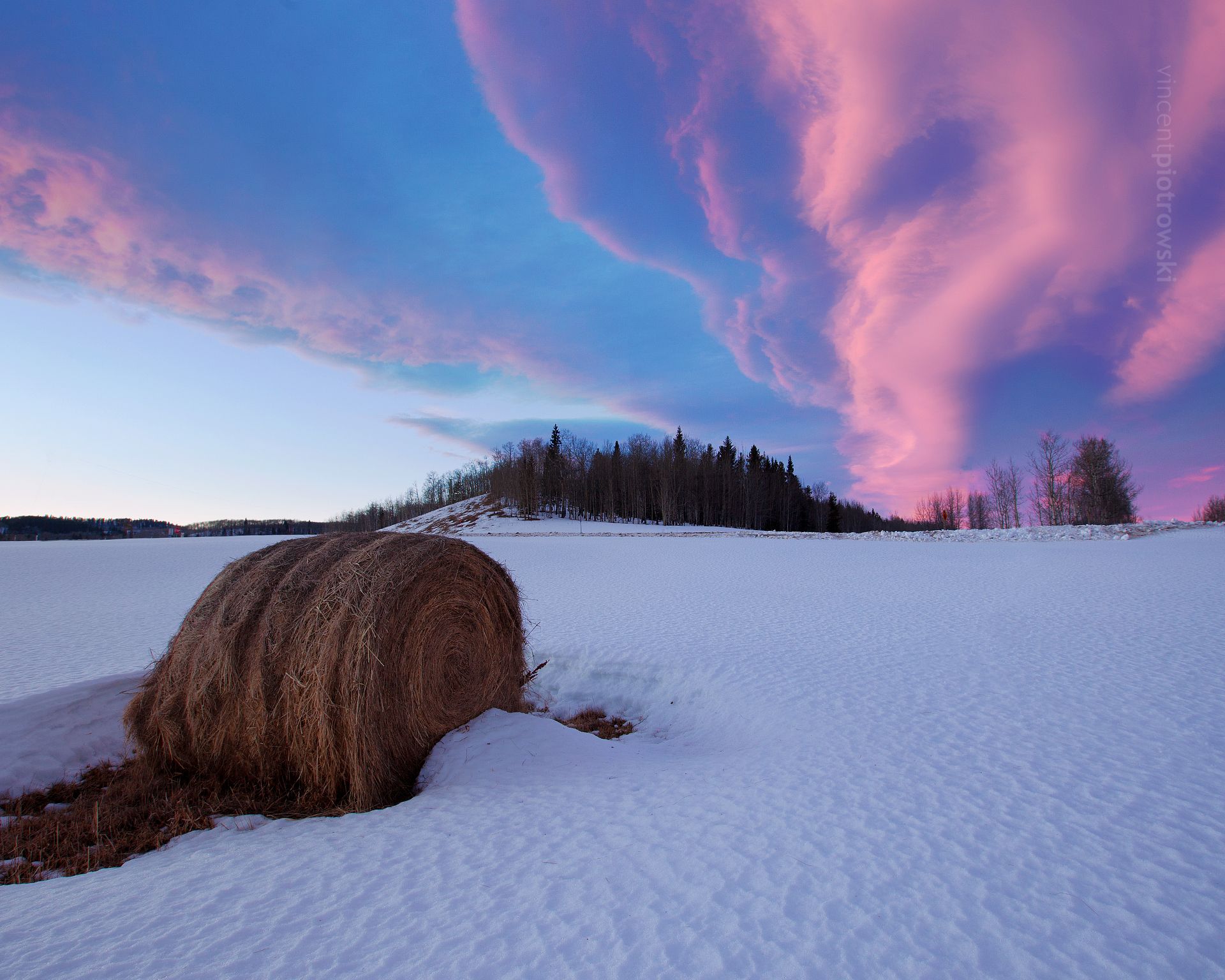 A round bale of hay in the snow under a spectacular cloud formation