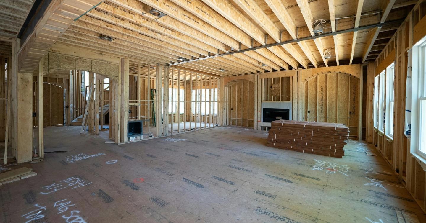 A new house at framing stage, with the floor joists overhead and notes written in marker on the subfloor.