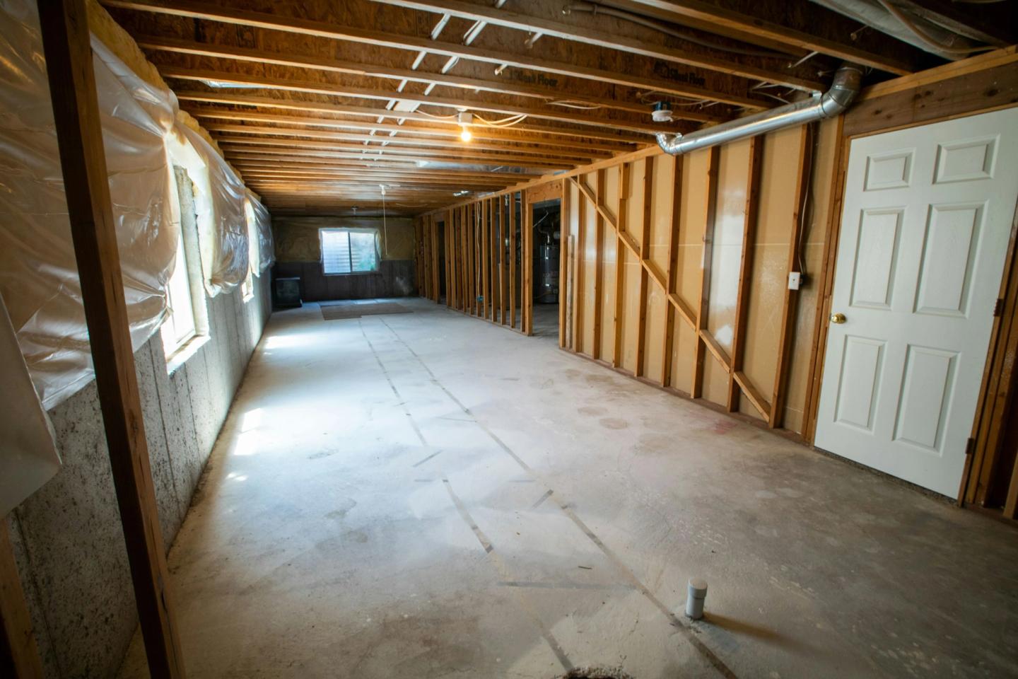 Unfinished basement with open wall framing, poly vapour barrier and exposed ductwork before drywall