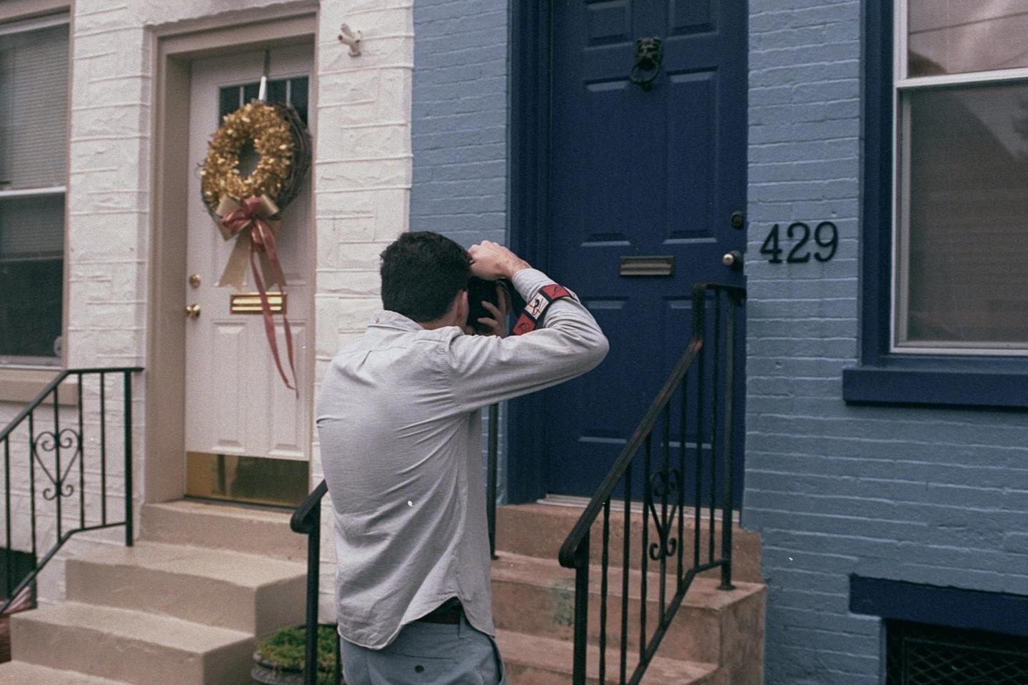 A man photographing the front door and entrance of a house with a camera.