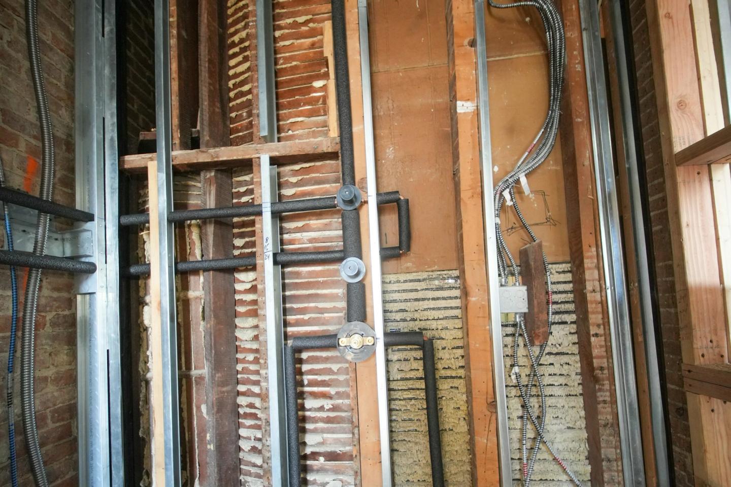 Open bathroom wall with plumbing pipes, electrical wiring and a junction box exposed before drywall